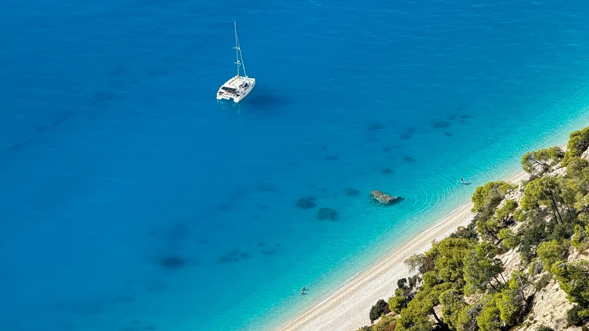 Vista aérea de una costa turquesa con veleros, representando los destinos de Taormina Travel
