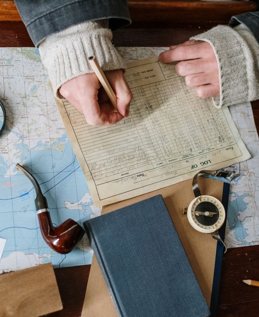 Manos escribiendo un itinerario de viaje a mano sobre un mapa, con brújula y libreta